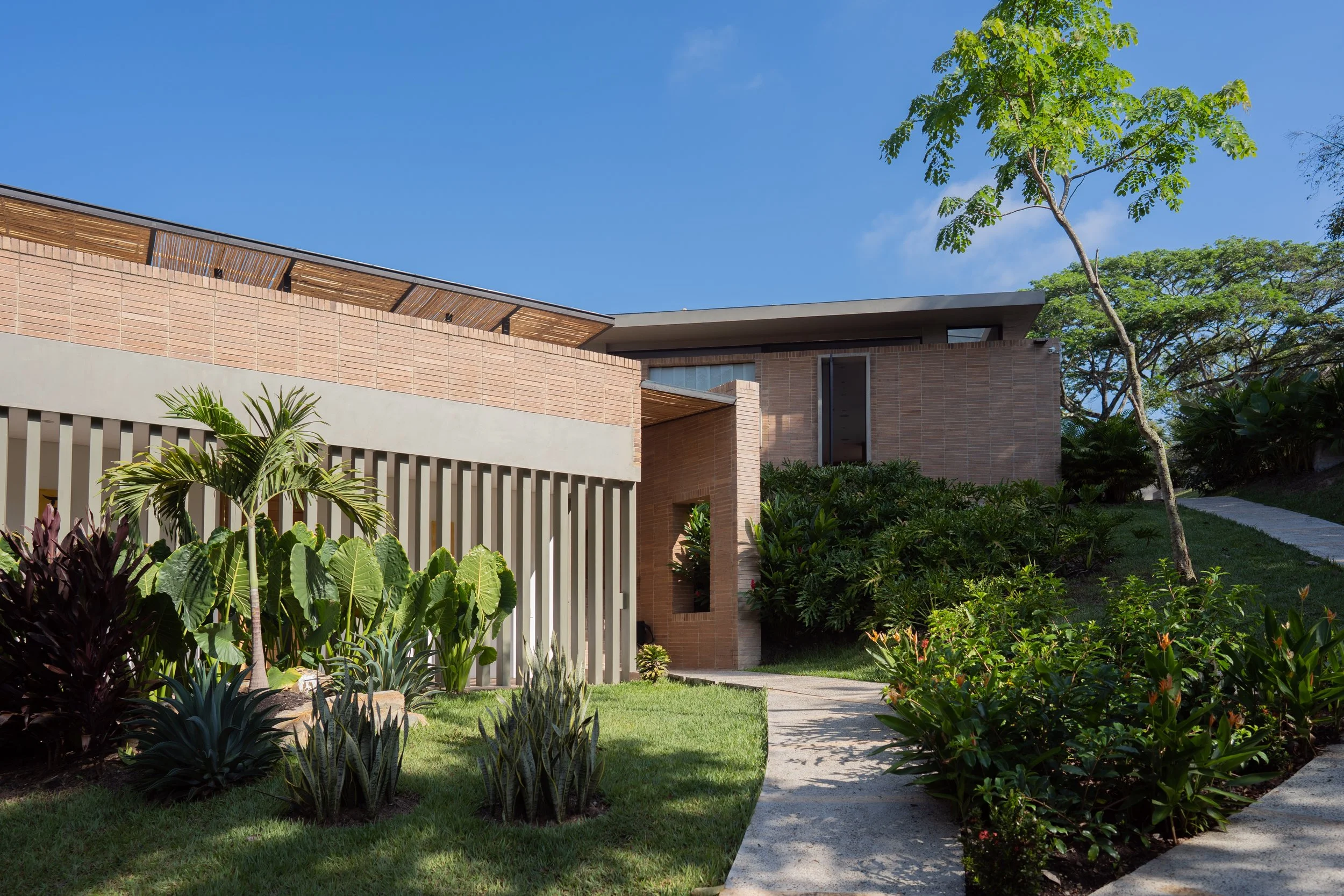 Casa de ladrillo a la vista con celosía de concreto entre jardines tropicales